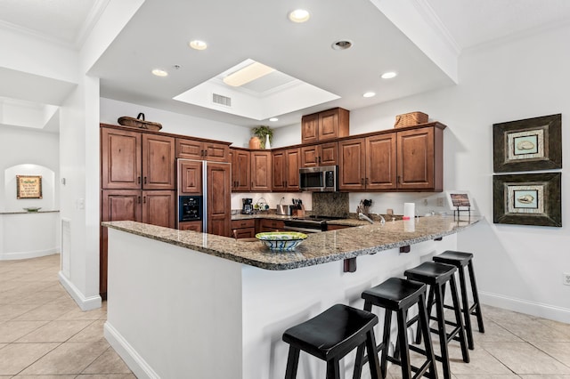 kitchen with dark stone countertops, appliances with stainless steel finishes, kitchen peninsula, a kitchen breakfast bar, and ornamental molding