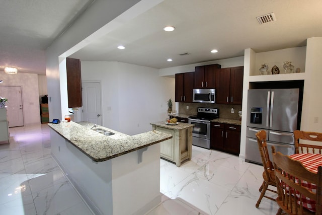 kitchen featuring tasteful backsplash, light stone counters, a kitchen island, appliances with stainless steel finishes, and a breakfast bar area