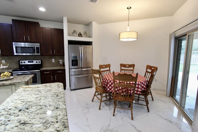 kitchen with plenty of natural light, pendant lighting, light stone countertops, and appliances with stainless steel finishes