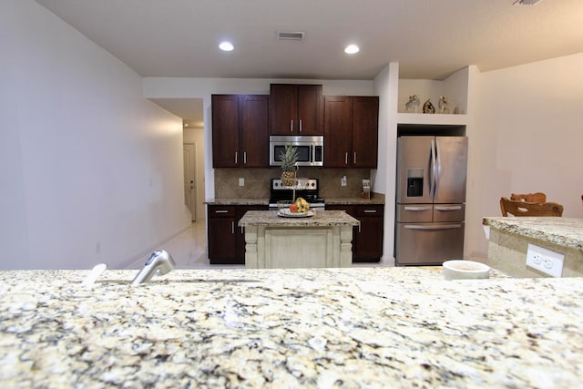 kitchen featuring dark brown cabinets, stainless steel appliances, light stone counters, a center island, and decorative backsplash