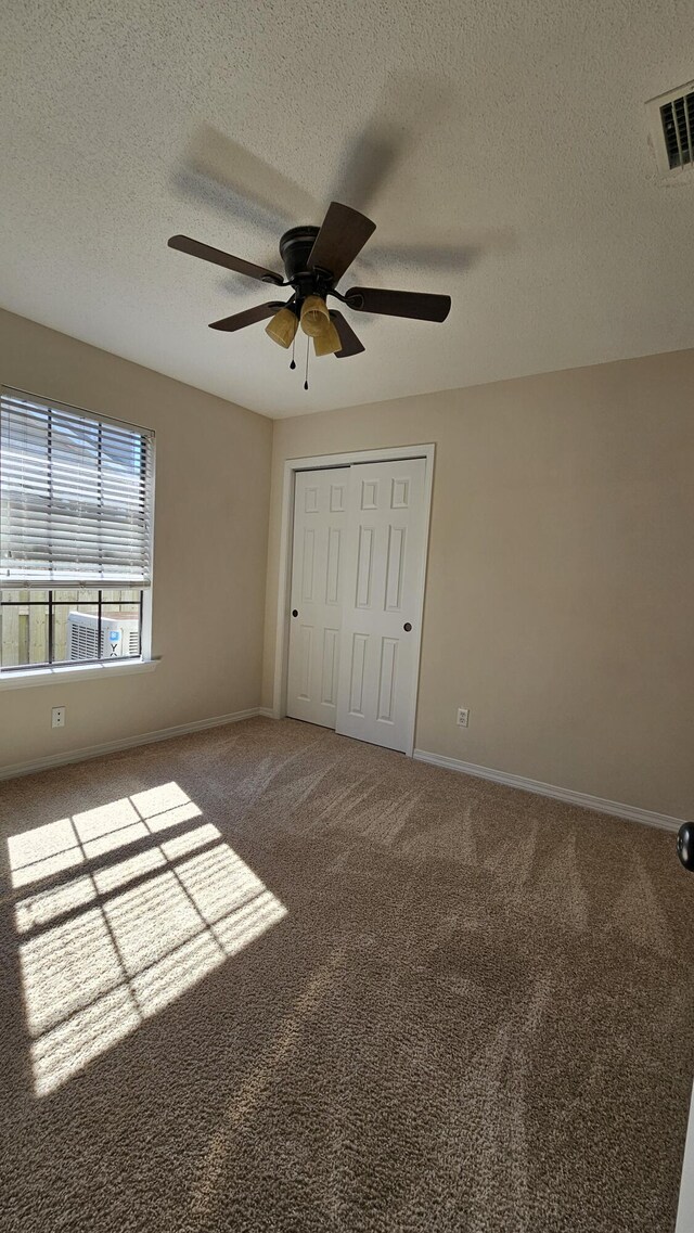 unfurnished bedroom with a closet, ceiling fan, carpet floors, and a textured ceiling