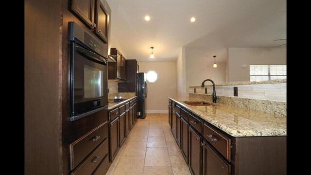 kitchen featuring decorative light fixtures, light stone countertops, sink, black appliances, and tasteful backsplash