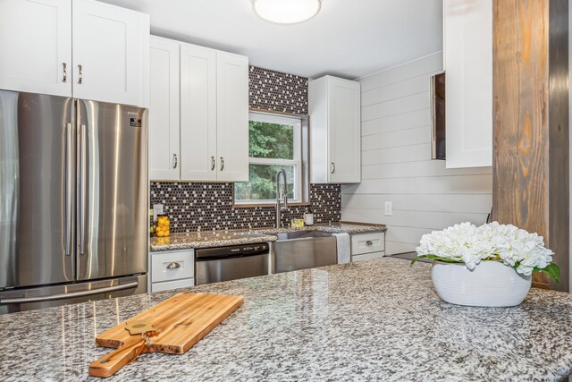 kitchen featuring appliances with stainless steel finishes, white cabinetry, light stone countertops, and decorative backsplash