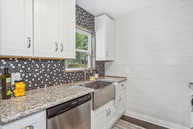 kitchen with white cabinets, dishwasher, light stone counters, sink, and wood walls