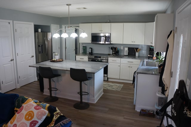 kitchen featuring dark wood-type flooring, stainless steel appliances, decorative light fixtures, and white cabinets