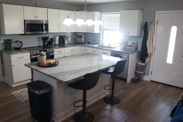 kitchen with white cabinets, hanging light fixtures, a kitchen island, appliances with stainless steel finishes, and dark hardwood / wood-style floors