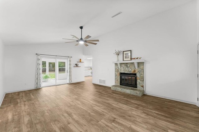 unfurnished living room with lofted ceiling, ceiling fan, a stone fireplace, and wood-type flooring