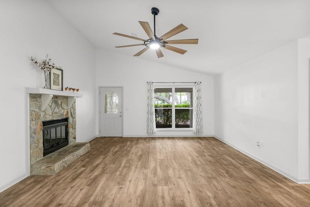 unfurnished living room featuring ceiling fan, hardwood / wood-style flooring, vaulted ceiling, and a stone fireplace