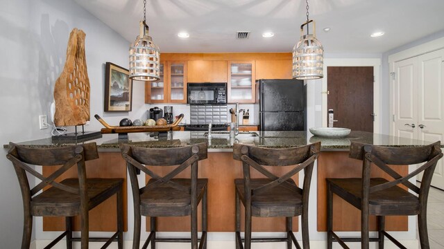 kitchen featuring decorative light fixtures, black appliances, a kitchen breakfast bar, and dark stone counters