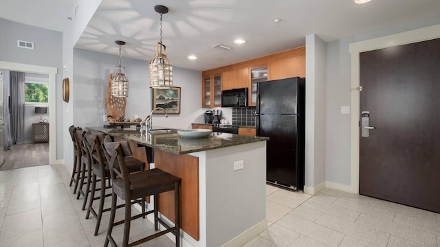 kitchen featuring light tile patterned flooring, sink, a breakfast bar area, dark stone countertops, and black appliances