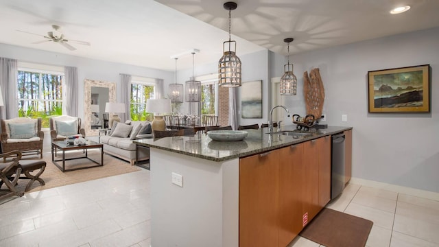 kitchen with decorative light fixtures, black dishwasher, sink, dark stone counters, and light tile patterned floors