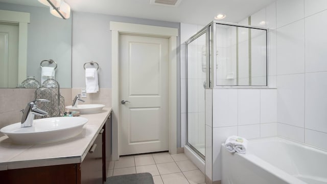 bathroom with tile patterned floors, independent shower and bath, vanity, and tile walls