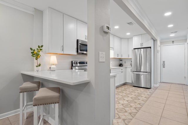 kitchen with a breakfast bar, crown molding, tasteful backsplash, white cabinetry, and stainless steel appliances