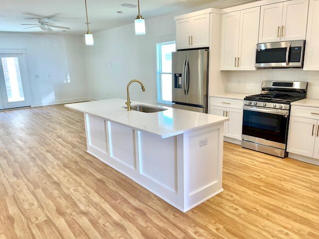 kitchen with a kitchen island with sink, sink, white cabinets, decorative light fixtures, and appliances with stainless steel finishes