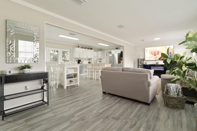 living room featuring wood-type flooring, crown molding, and sink