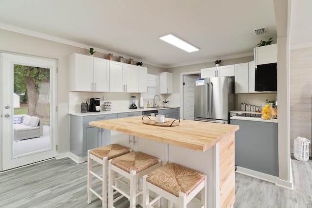 kitchen with a kitchen bar, stainless steel refrigerator, sink, wooden counters, and white cabinets