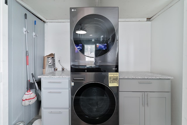 laundry room featuring stacked washer and clothes dryer and cabinets