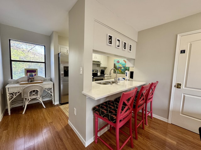 kitchen with white cabinetry, sink, stainless steel appliances, a breakfast bar, and hardwood / wood-style flooring