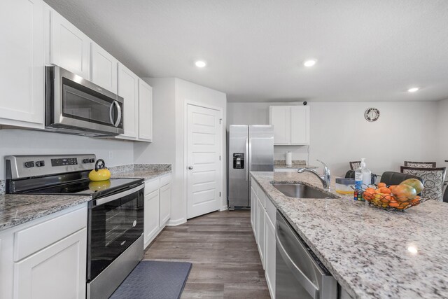 kitchen with white cabinets, hardwood / wood-style flooring, light stone countertops, stainless steel appliances, and sink