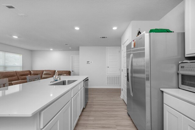 kitchen featuring light wood-type flooring, appliances with stainless steel finishes, white cabinetry, sink, and a kitchen island with sink