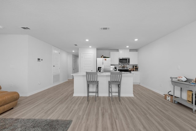 kitchen with white cabinets, visible vents, light wood finished floors, stainless steel appliances, and a center island with sink