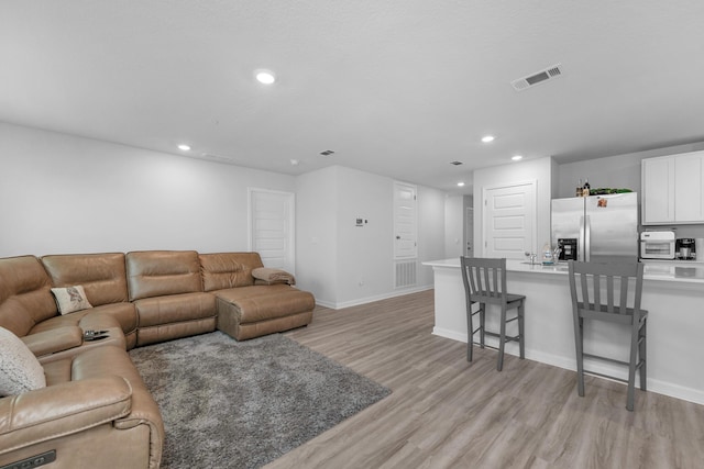 living room featuring baseboards, visible vents, light wood-style flooring, and recessed lighting