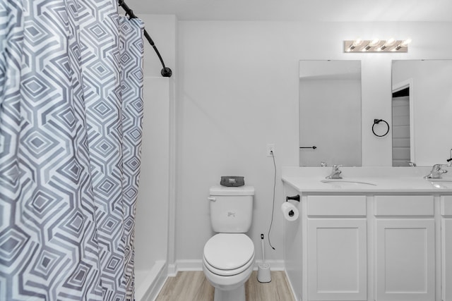 bathroom with a shower with shower curtain, toilet, a sink, wood finished floors, and double vanity