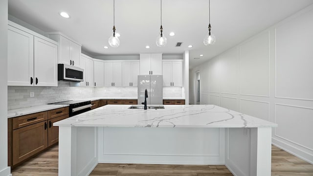 kitchen featuring appliances with stainless steel finishes, white cabinetry, a kitchen island with sink, and light stone counters