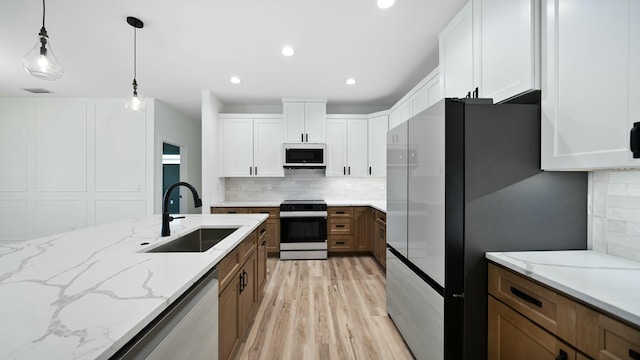 kitchen featuring white cabinets, sink, light stone countertops, decorative light fixtures, and stainless steel appliances