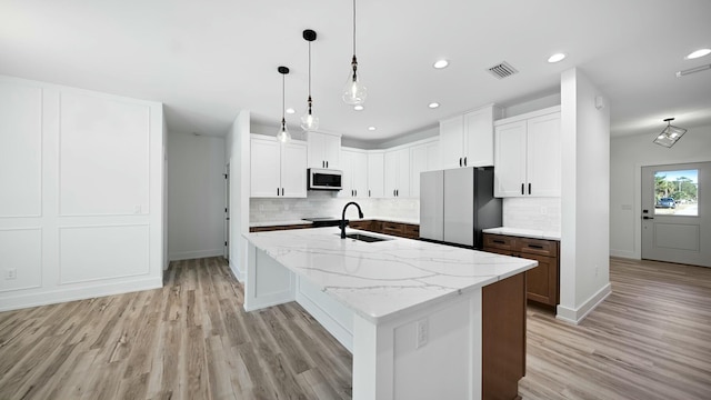 kitchen with light stone counters, stainless steel appliances, white cabinetry, and an island with sink