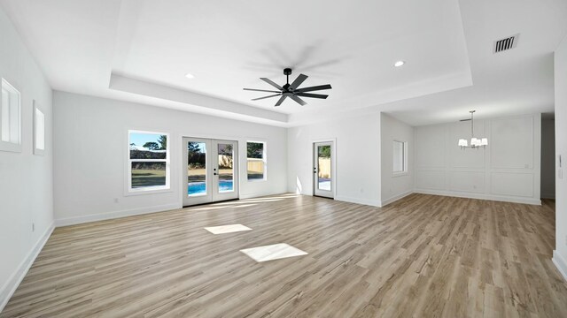 unfurnished living room with a tray ceiling, light hardwood / wood-style flooring, and ceiling fan with notable chandelier