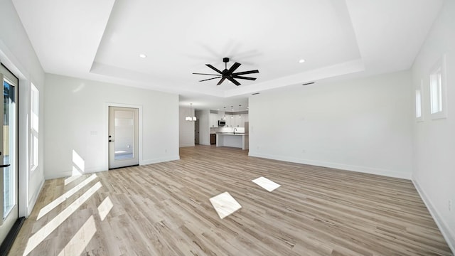 unfurnished living room with ceiling fan, light hardwood / wood-style floors, and a tray ceiling