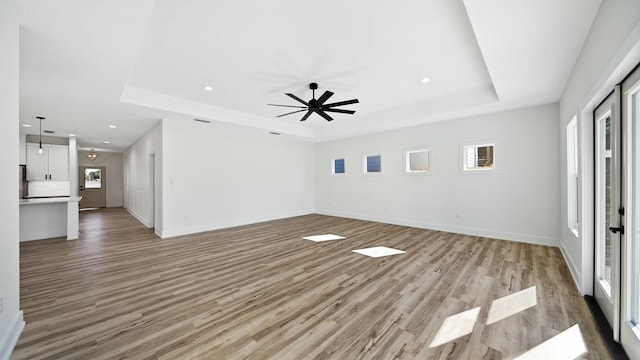 unfurnished living room featuring a raised ceiling, light hardwood / wood-style flooring, a wealth of natural light, and ceiling fan