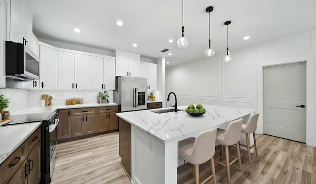 kitchen with white cabinetry, pendant lighting, light hardwood / wood-style floors, a kitchen island with sink, and appliances with stainless steel finishes