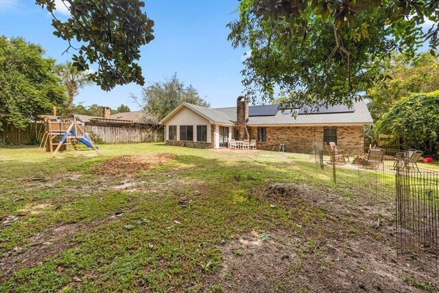 2205 Calle De Marbella, Navarre, FL 32566 - back of property featuring a lawn, a patio, a fenced backyard, a playground, and solar panels