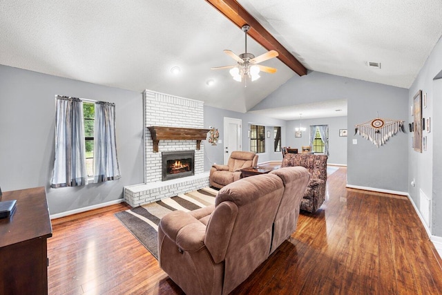 living room featuring a fireplace, ceiling fan with notable chandelier, a textured ceiling, wood-type flooring, and vaulted ceiling with beams