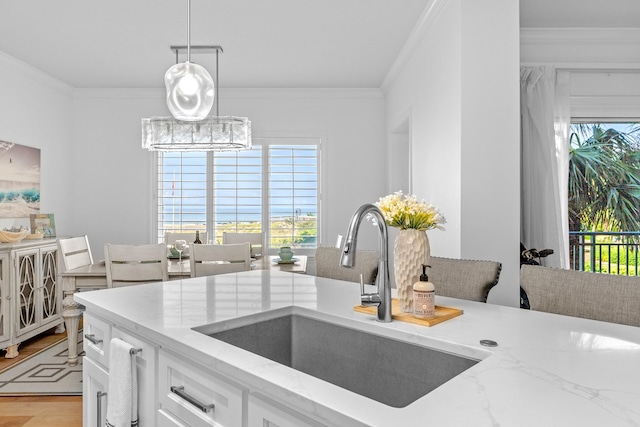 kitchen featuring decorative light fixtures, light hardwood / wood-style flooring, ornamental molding, sink, and white cabinets