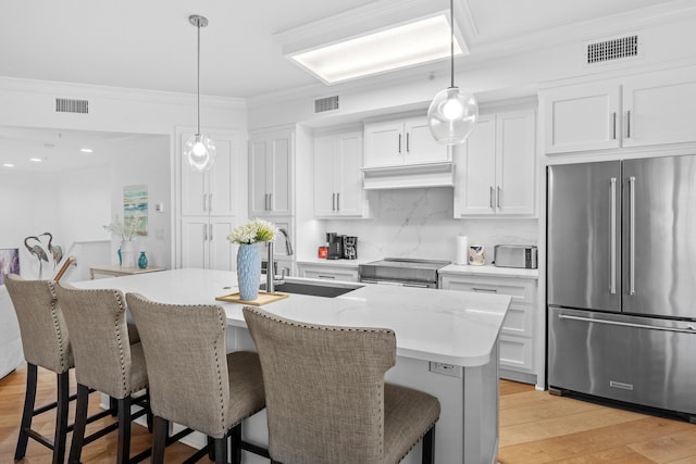 kitchen with a kitchen island with sink, stainless steel appliances, sink, light wood-type flooring, and white cabinets