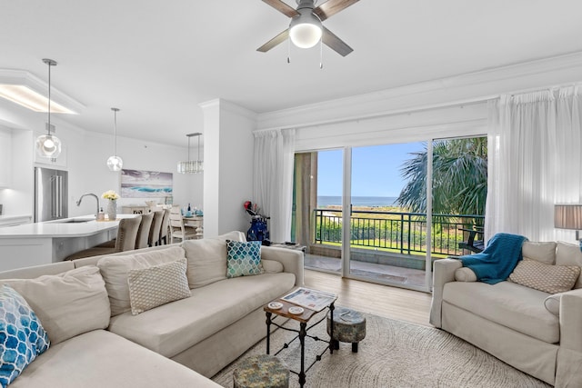 living room with light hardwood / wood-style flooring, ornamental molding, sink, ceiling fan, and a water view