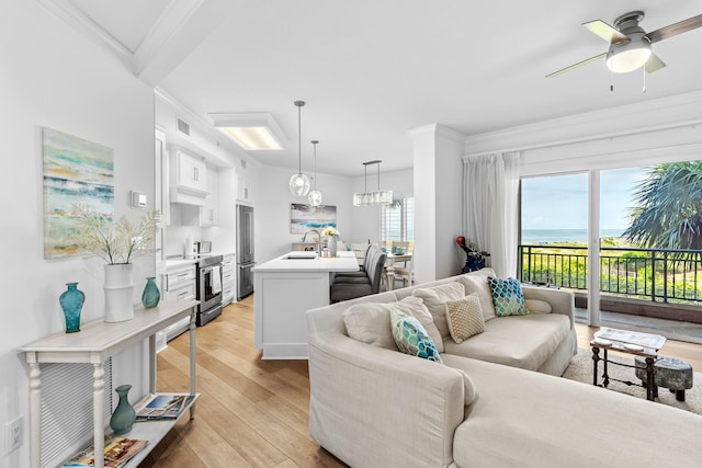 living room featuring crown molding, light wood-type flooring, ceiling fan with notable chandelier, sink, and a water view