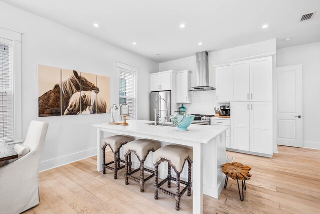 kitchen featuring an island with sink, white cabinets, and wall chimney range hood