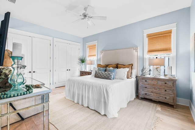 bedroom featuring light hardwood / wood-style flooring, multiple closets, ceiling fan, and multiple windows