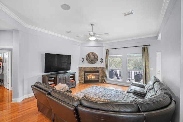 living room with light wood-type flooring, ceiling fan, ornamental molding, and a stone fireplace