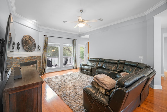 living room with crown molding, wood-type flooring, ceiling fan, and a stone fireplace