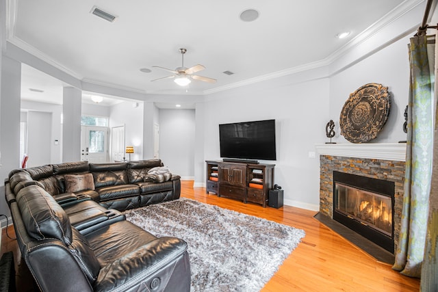 living room featuring crown molding, hardwood / wood-style flooring, ceiling fan, and a stone fireplace