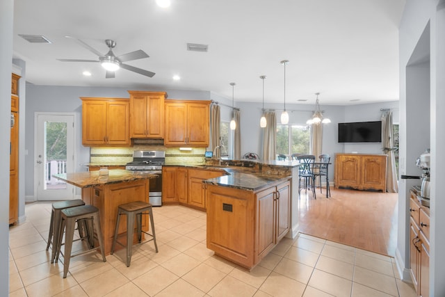 kitchen with ceiling fan with notable chandelier, decorative light fixtures, a kitchen breakfast bar, kitchen peninsula, and gas stove