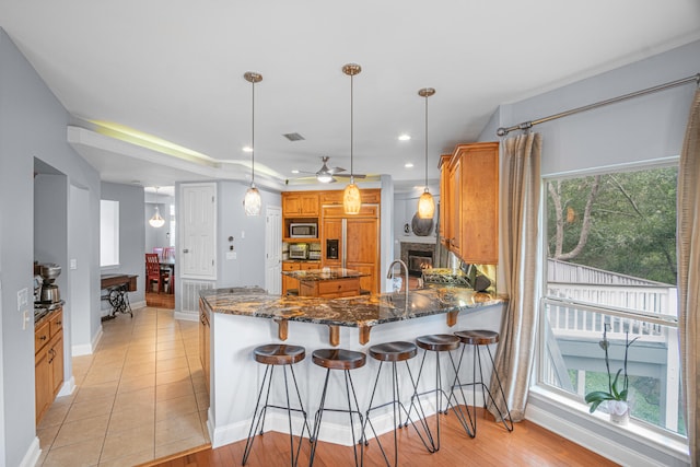 kitchen with dark stone counters, decorative light fixtures, kitchen peninsula, stainless steel microwave, and light hardwood / wood-style floors