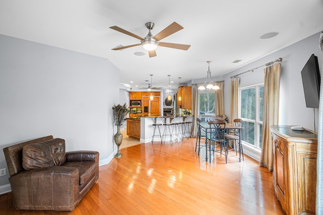 living room with ceiling fan with notable chandelier and light wood-type flooring