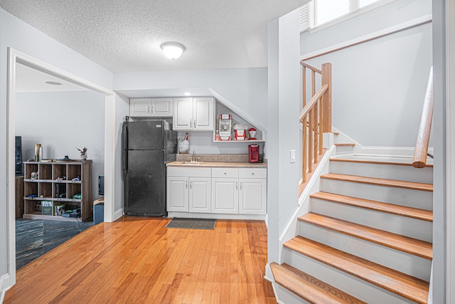 interior space with a textured ceiling, sink, black refrigerator, light wood-type flooring, and white cabinets