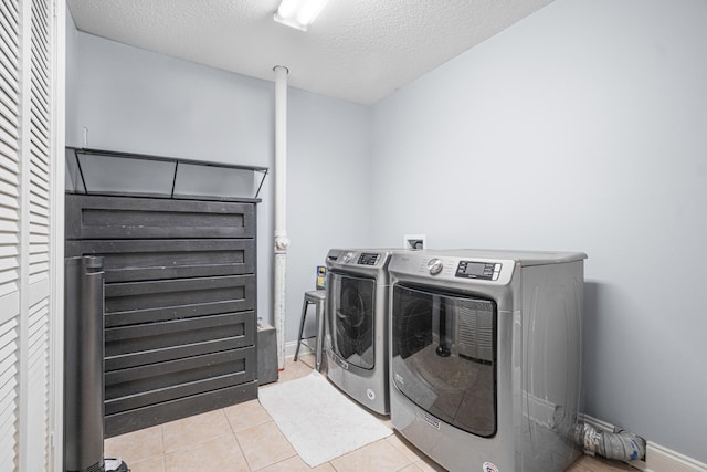 laundry room featuring washing machine and clothes dryer, light tile patterned floors, and a textured ceiling